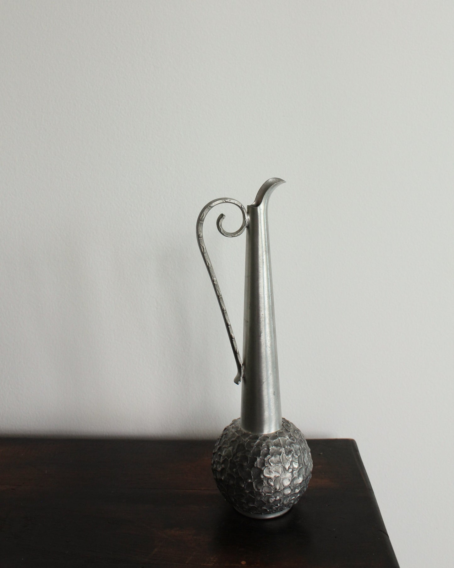 Silver vase with textured base on a dark surface against a light background