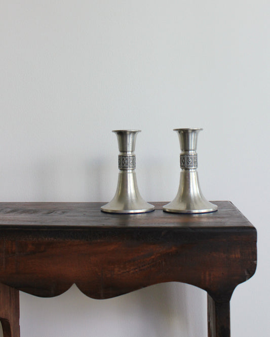Two silver candle holders on a wooden table with a plain background