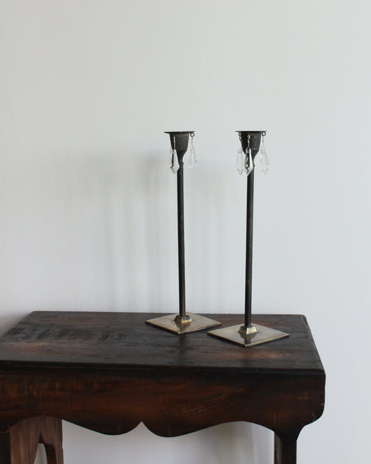 Two silver candle holders with crystal accents on a wooden table against a plain background