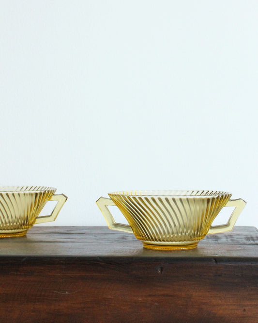 Two yellow glass bowls with handles on a wooden surface.