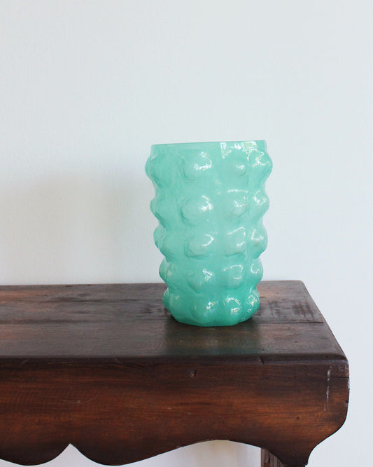 Green textured vase on a wooden surface with a white background