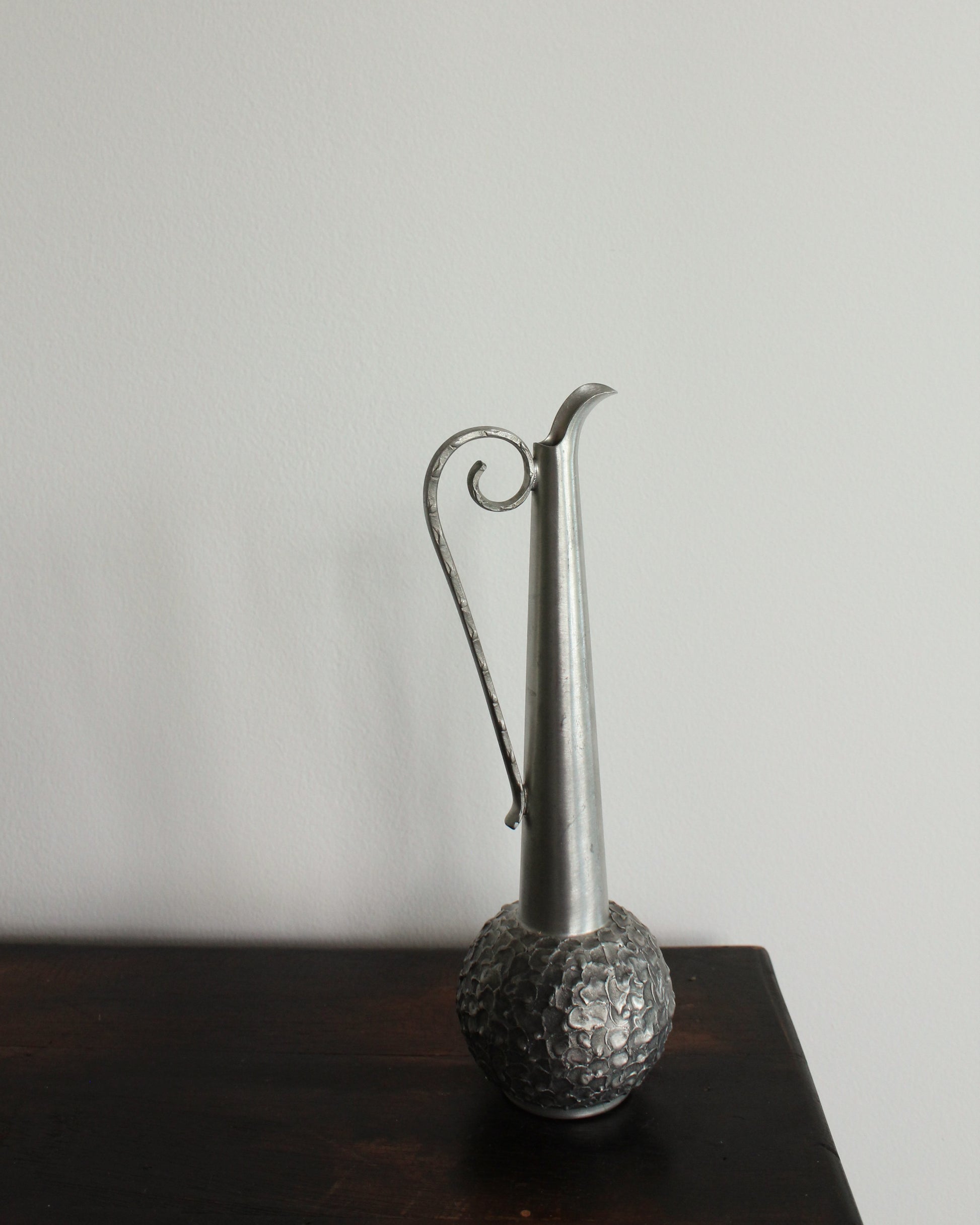 Silver vase with textured base on a dark surface against a light background