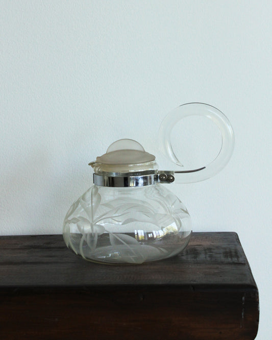 Clear glass teapot with a white lid on a wooden surface against a light gray background